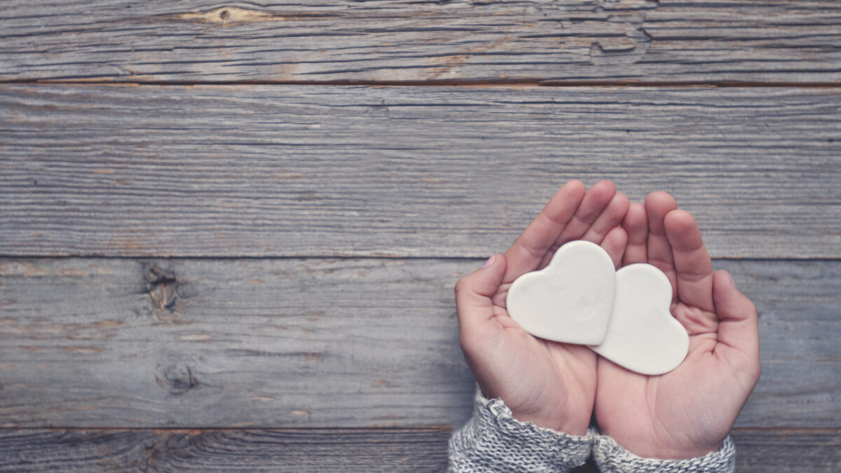 Woman holding two white love hearts. A woman is holding them in her hands. There is a rustic wood table underneath her hands. Valentines day or anniversary concept. Copy space.