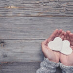 Woman holding two white love hearts. A woman is holding them in her hands. There is a rustic wood table underneath her hands. Valentines day or anniversary concept. Copy space.