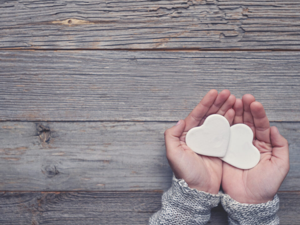 Woman holding two white love hearts. A woman is holding them in her hands. There is a rustic wood table underneath her hands. Valentines day or anniversary concept. Copy space.