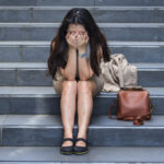 young depressed and desperate Asian Korean businesswoman crying alone sitting on street staircase suffering stress and depression crisis being victim of mobbing or fired losing her job